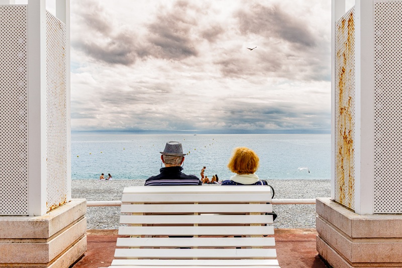 2 personen in rugaanzicht zitten op een bank aan zee