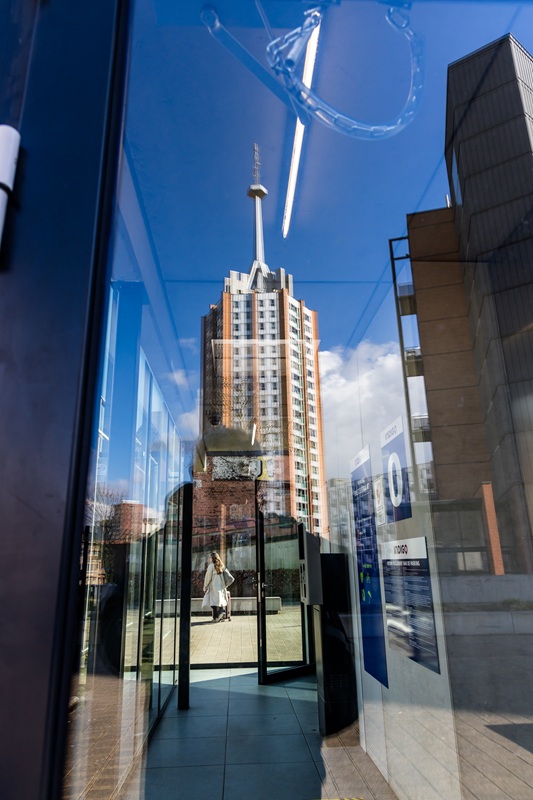 Een flatgebouw in Leuven weerspiegeld in glas